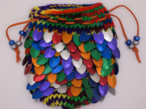 Dragon scale dice bag knitted with red, orange, green, blue, purple, and silver metallic scales made from rainbow colored yarn.