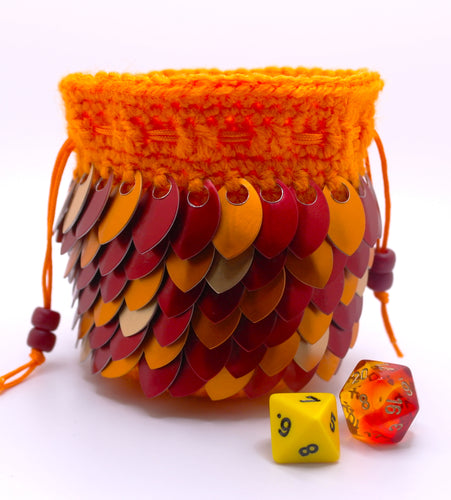 Dice bag made from orange yarn with red, orange, and gold metallic scales representing a red dragon with an orange drawstring closure.