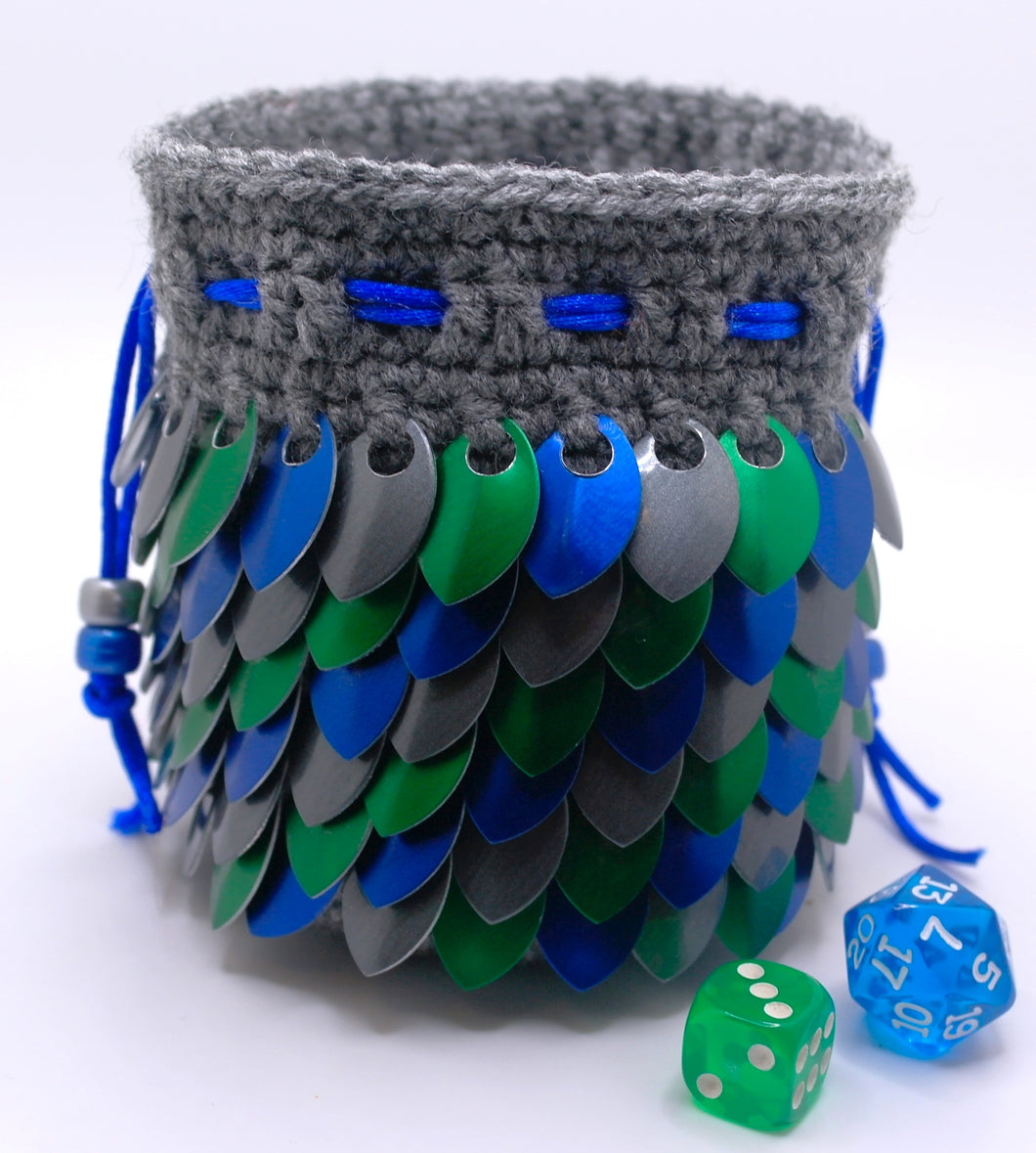 Dice bag made from gray yarn with blue, green, and graphite metallic dragon scales and a blue drawstring