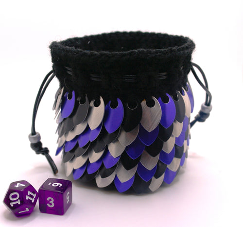 Dice bag made with black yarn and purple, silver, and black metallic scales with a black drawstring closure